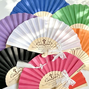 May include: A selection of colourful paper fans in blue, green, orange, pink, purple, white, and black. Each fan has a wooden handle and features the text "This is the day that the Lord has made" and "Psalm 118:24". Some fans are decorated with bows.