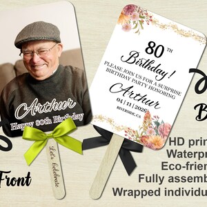 May include: Double-sided birthday fan with a photo of a man on the front and event details on the back. The front has the text "Arthur Happy 80th Birthday". The back has the text "80th Birthday!" and event details. Includes a green bow.