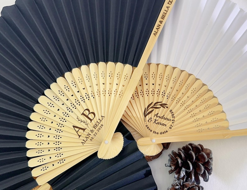 May include: Wooden hand fans with laser-cut floral designs and personalized text. One fan is black, another is white, and two are natural wood. The text includes names and dates, ideal for wedding favors.