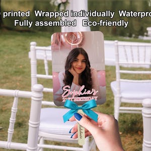 May include: A personalized fan featuring a photo of a young woman, with the text "Sophia's 21st Birthday." The fan has a teal bow and a wooden handle. The image is printed on a rectangular card.