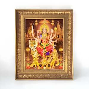 Peut inclure: Une impression d'art encadrée représentant une divinité aux bras multiples assise sur un tigre. La figure porte des bijoux dorés ornés et un vêtement rouge et or. L'arrière-plan montre une architecture de temple, des lampes et un dais doré.