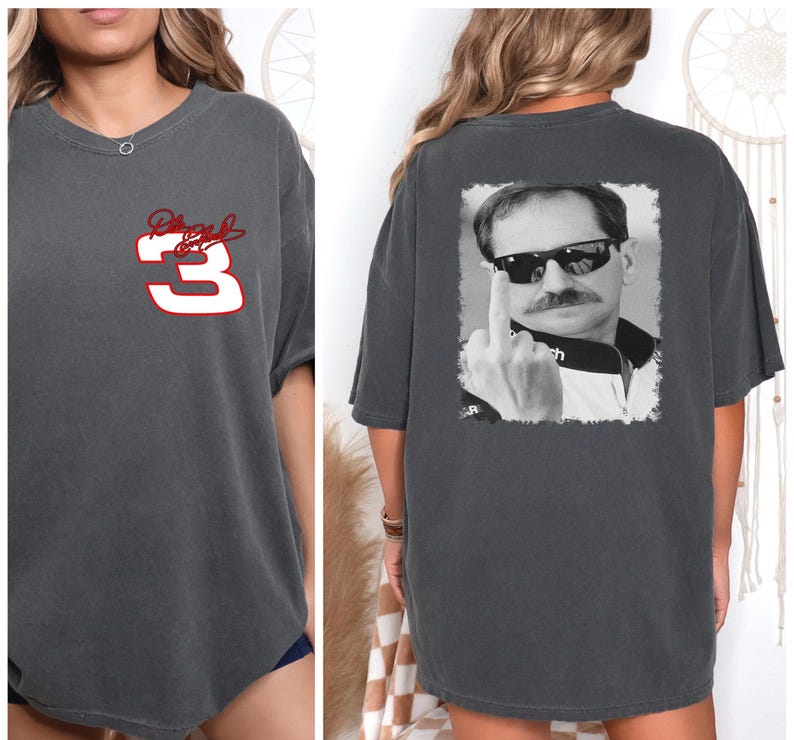 Puede incluir: Una camiseta gris oscura de gran tama&ntilde;o con un n&uacute;mero 3 rojo y una firma en la parte delantera. La parte posterior de la camiseta presenta una foto en blanco y negro de un hombre con gafas de sol y haciendo el dedo medio.