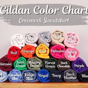 Pu&ograve; includere: Una tabella colori per felpe girocollo Gildan, che mostra una variet&agrave; di campioni di tessuto arrotolati. I colori includono bianco, cenere, grigio sportivo, sabbia, rosa chiaro, rosso, arancione, oro, ecc. Il testo "Gildan Color Chart Crewneck Sweatshirt" &egrave; in alto.