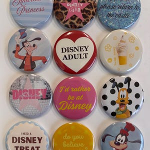 Op de afbeelding: Een verzameling van twaalf ronde Disney-thema buttons. De buttons tonen verschillende ontwerpen, waaronder teksten als "America's Princess", "Disney Girl" en "I'd rather be at Disney". Sommige buttons tonen Disney-personages en -iconen.