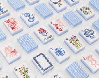 May include: A collection of rectangular mahjong tiles with white faces and light blue backs. The tiles feature various colorful illustrations including red ribbons, green bamboo stalks, blue circular patterns, a person with sunglasses, and the word JOKER.