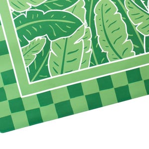 May include: A green and white patterned textile featuring a tropical leaf design. The border has a checkered pattern in shades of green. The design includes a white border and the artist's signature.
