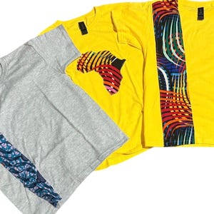 Puede incluir: Tres camisetas de manga corta. Una es gris con un diseño azul y morado estampado en la manga izquierda. Las otras dos son amarillas. Una camiseta amarilla tiene un gráfico de África y la otra un diseño vertical colorido.