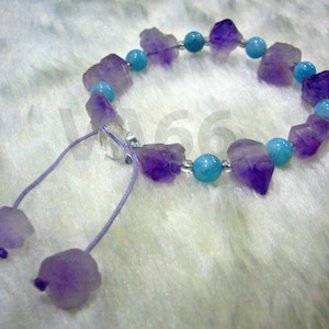 以下が含まれることがあります： 銀色の留め具とリボン留めが付いた、紫と青の宝石のブレスレット。ブレスレットは、ファセットカットされたアメジストとターコイズの石で作られています。