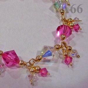 Könnte beinhalten: Ein goldenes Kettenarmband mit rosa und klaren Kristallperlen. Das Armband hat einen Anhänger mit mehreren rosa und klaren Kristallperlen.