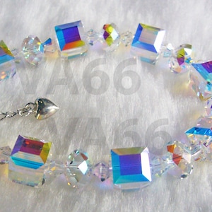 Könnte beinhalten: Ein Armband aus klaren Kristallen mit schillernden, quadratischen und runden Perlen. Das Armband hat eine silberfarbene Kette und einen herzförmigen Anhänger. Die Kristalle reflektieren einen Regenbogen an Farben.