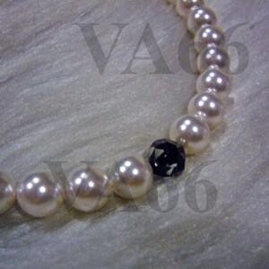 Peut inclure: Un collier de perles blanches avec un accent de pierre précieuse noire. Le collier est sur un fond de tissu blanc.