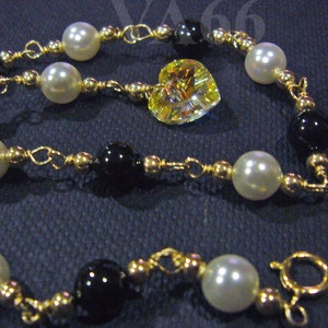 May include: A gold chain bracelet with black and white beads and a heart-shaped crystal charm.