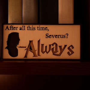 Könnte beinhalten: Holzschild mit dem Zitat "After all this time, Severus? Always" in schwarzer Schrift. Das Schild zeigt eine Silhouette eines Kopfes und wird auf einem Regal mit Büchern im Hintergrund ausgestellt. Das Schild ist aus hellem Holz gefertigt.
