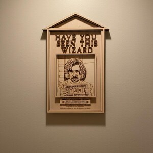 Peut inclure: Décoration murale en bois représentant une affiche de recherche de sorcier. L'enseigne indique « Avez-vous vu ce sorcier » au-dessus d'une image encadrée d'un homme. L'affiche comprend le texte « Prison d'Azkaban » et le numéro « 39 ».