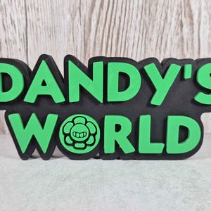 May include: Black and green 3D printed sign that reads "DANDY'S WORLD" with a green cartoon character in the middle.
