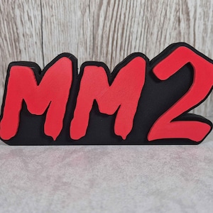 Può includere: Un cartello stampato in 3D nero e rosso che dice "MM2". Le lettere sono in un carattere grassetto e stilizzato.