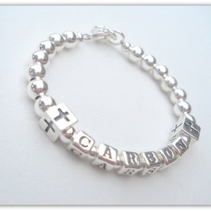 May include: Silver beaded bracelet with a cross charm and the name "CARSON" spelled out in silver beads.