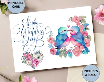 Op de afbeelding: Printbare trouwkaart met een aquarel-illustratie van twee blauwe vogels die elkaar kussen in een bloemenkrans. De tekst "Happy Wedding Day" is in cursief geschreven.
