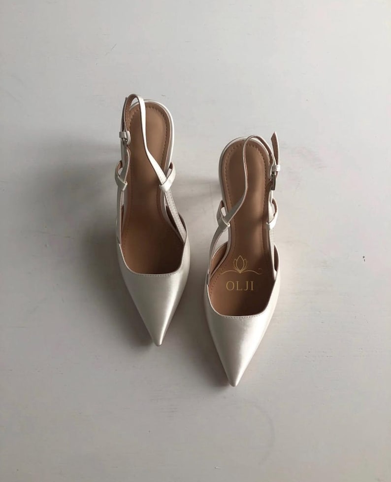 Puede incluir: Un par de zapatos de tac&oacute;n slingback de color marfil con punta. Los zapatos tienen correas finas y cierre de hebilla. El interior es de color marr&oacute;n claro y el nombre de la marca "OLJI" est&aacute; impreso en la plantilla.