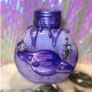 May include: A purple potion bottle with a metallic, iridescent finish. The bottle features a label with the words "Mystic Moon" and a planet design. Decorative charms include a crescent moon and a star. The bottle's cap has a dripped effect.