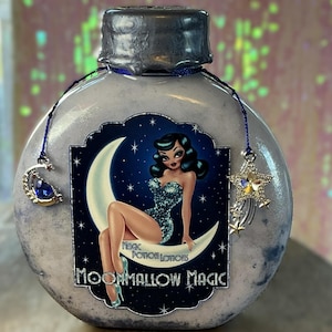 May include: A round, light blue bottle with a silver cap and a blue cord with charms. The label features a woman sitting on a crescent moon with the text "Moonmallow Magic" and "Magic Potion Lotions".
