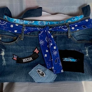 May include: A blue denim tote bag with a blue bandana pattern trim and a blue bandana tied around the top. The bag has a patch that says "Biker" with a small American flag on it.