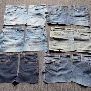 May include: A collection of denim skirts in various shades of blue, arranged on a textured surface. The skirts have classic five-pocket designs, with visible stitching and metal hardware. Some skirts show signs of wear and tear, adding to their vintage appeal.