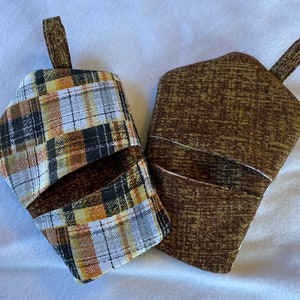May include: Two quilted oven mitts. One features a plaid pattern in brown, black, yellow, and white. The other has a brown textured fabric. Both have a loop for hanging.