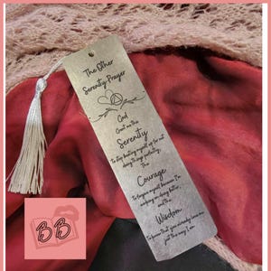 May include: A silver bookmark with a black inscription of "The Other Serenity Prayer" and a triangle symbol. The text reads "God grant me the serenity to stop beating myself up for not doing things perfectly, the courage to forgive myself because I'm working on doing better, and the wisdom to know that you already love me just the way I am."