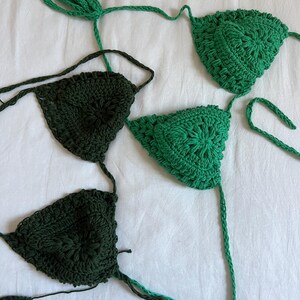May include: Two crocheted bikini tops in green and dark green. The tops are made with a delicate, intricate pattern.