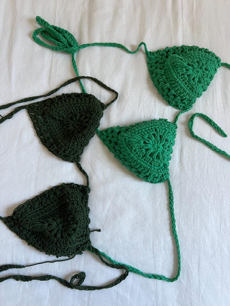May include: Two crocheted bikini tops in green and dark green. The tops are made with a delicate, intricate pattern.
