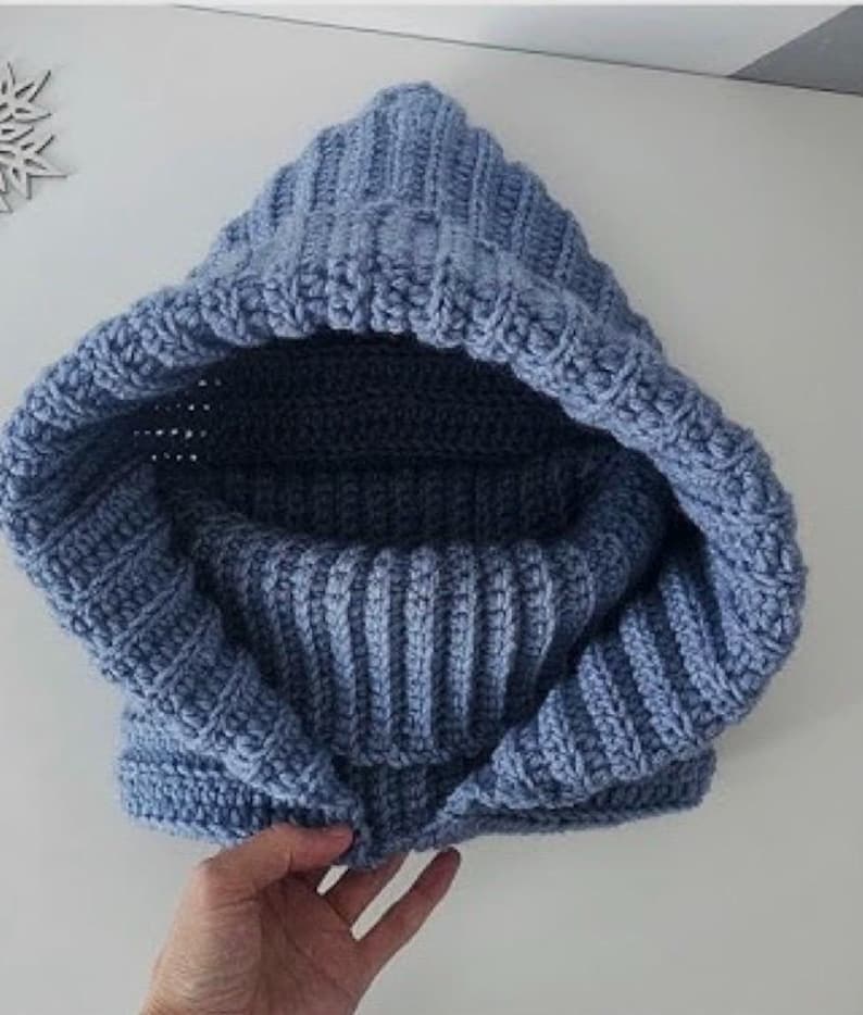 Op de afbeelding: Een blauwe gehaakte capuchon met een geribbelde textuur. De capuchon is dubbelgevouwen en de capuchon is binnenstebuiten gekeerd.