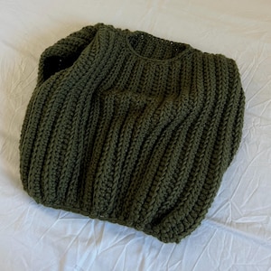 May include: An olive green, hand-knitted sweater. The sweater has a ribbed design across the body and sleeves. The neckline is a simple crew neck. The garment is made of a thick, textured yarn, giving it a cosy appearance.