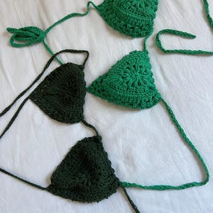 May include: Two crocheted bikini tops, one in a dark green and one in a lighter green. The tops are made with a delicate, intricate stitch pattern.