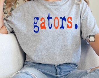 Puede incluir: Una camiseta gris jaspeado de manga corta con la palabra gators. impresa en el pecho en letras alternas azules y naranjas. El texto incluye un punto al final, con las letras g, t, r y el punto en azul, y las letras a, o, s en naranja.