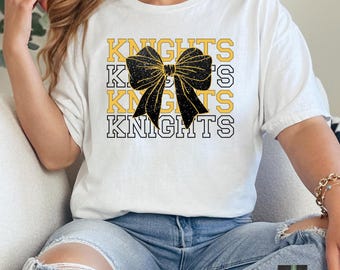 Puede incluir: Camiseta blanca con un lazo de brillo negro y dorado y la palabra "Knights" repetida cuatro veces en un diseño apilado.