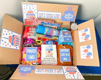 Puede incluir: Una caja de regalo de cartón llena de artículos de cumpleaños, incluyendo una lata de serpentinas, barras KitKat, una piñata pequeña y un kit de pastel en taza. Las solapas de la caja tienen gráficos impresos de cupcakes, globos y texto.