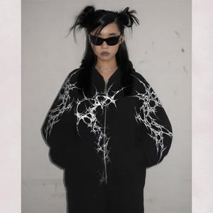May include: Black zip-up hoodie with a white, abstract design. The hoodie features a high collar and a full-length zipper. The words "high res" and "300 DPI" are visible in the image.