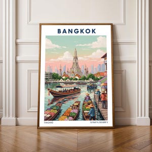 May include: A framed art print featuring a colorful illustration of Bangkok, Thailand. The image shows boats on a river, a tall temple, and the word "BANGKOK" at the top. The print includes the coordinates 13.7563° N 100.5018° E.