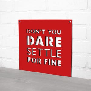 May include: Red metal sign with white text that reads "Don't you dare settle for fine".