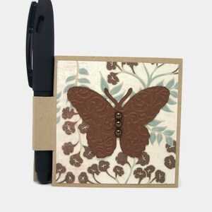 May include: A brown butterfly with a floral pattern on a beige notepad with a brown pen.
