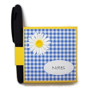May include: A yellow and blue gingham notepad with a white daisy and the word "Notes" in a white oval. A black pen is attached to the notepad.