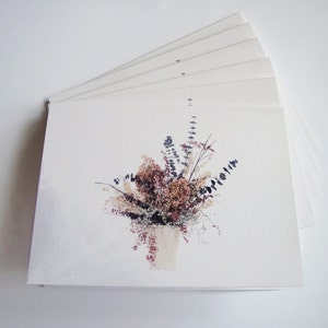 Puede incluir: Una pila de tarjetas de felicitaci&oacute;n en blanco con una imagen impresa de un ramo de flores secas en tonos marrones, beige y morados.