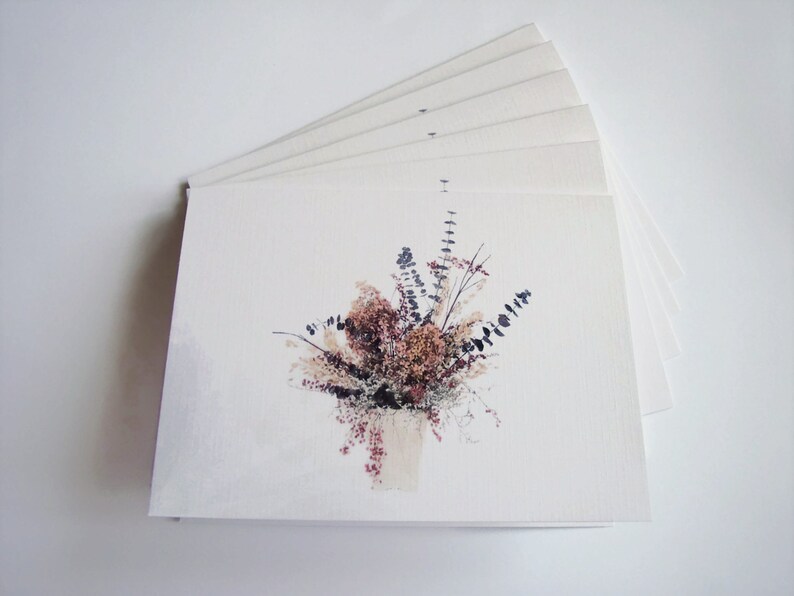 Puede incluir: Una pila de tarjetas de felicitaci&oacute;n en blanco con una imagen impresa de un ramo de flores secas en tonos marrones, beige y morados.