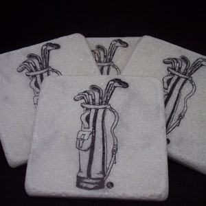 May include: Set of five square coasters with a golf theme. Each coaster features a black and white illustration of a golf bag filled with clubs. The coasters are made of a light-colored, textured material.
