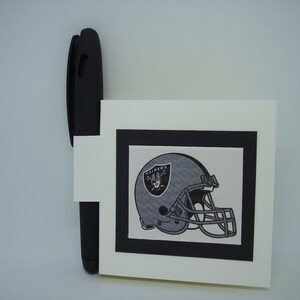 May include: A white card with a black border around a black and white image of a football helmet with the word "RAIDERS" on it.