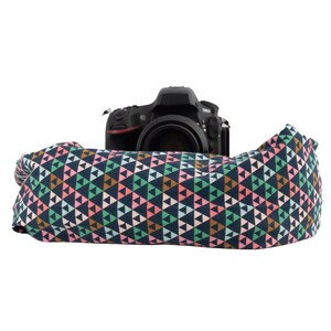 May include: A black DSLR camera with a patterned camera strap. The strap features a repeating geometric design of triangles in shades of navy, pink, green, and brown. The strap is made of fabric and is wrapped around the camera.