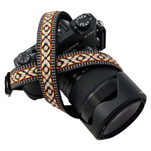 May include: A black camera with a lens and a colourful patterned camera strap. The camera has a dial with the text "X-T30" on it.