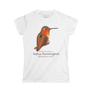 May include: White t-shirt featuring a watercolor illustration of a Rufous Hummingbird with a BlüMorpho tag. The bird is depicted in shades of orange, brown, and green, perched on a branch. The text "Rufous Hummingbird Selasphorus rufus" is printed below.