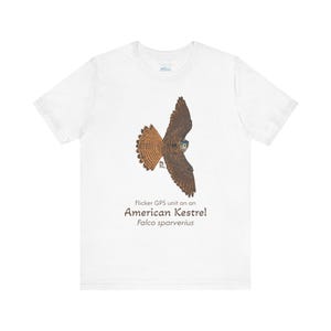 May include: White t-shirt with a brown and orange illustration of an American Kestrel in flight. The text "Flicker GPS unit on an American Kestrel Falco sparverius" is printed below the illustration.